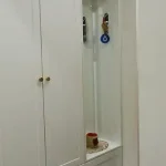 جالباسی نئوکلاسیک سفید با کلاف چوبی مشهود، شامل جا کفشی، آویز و نیمکت، در یک ورودی روشن و دکور شده.